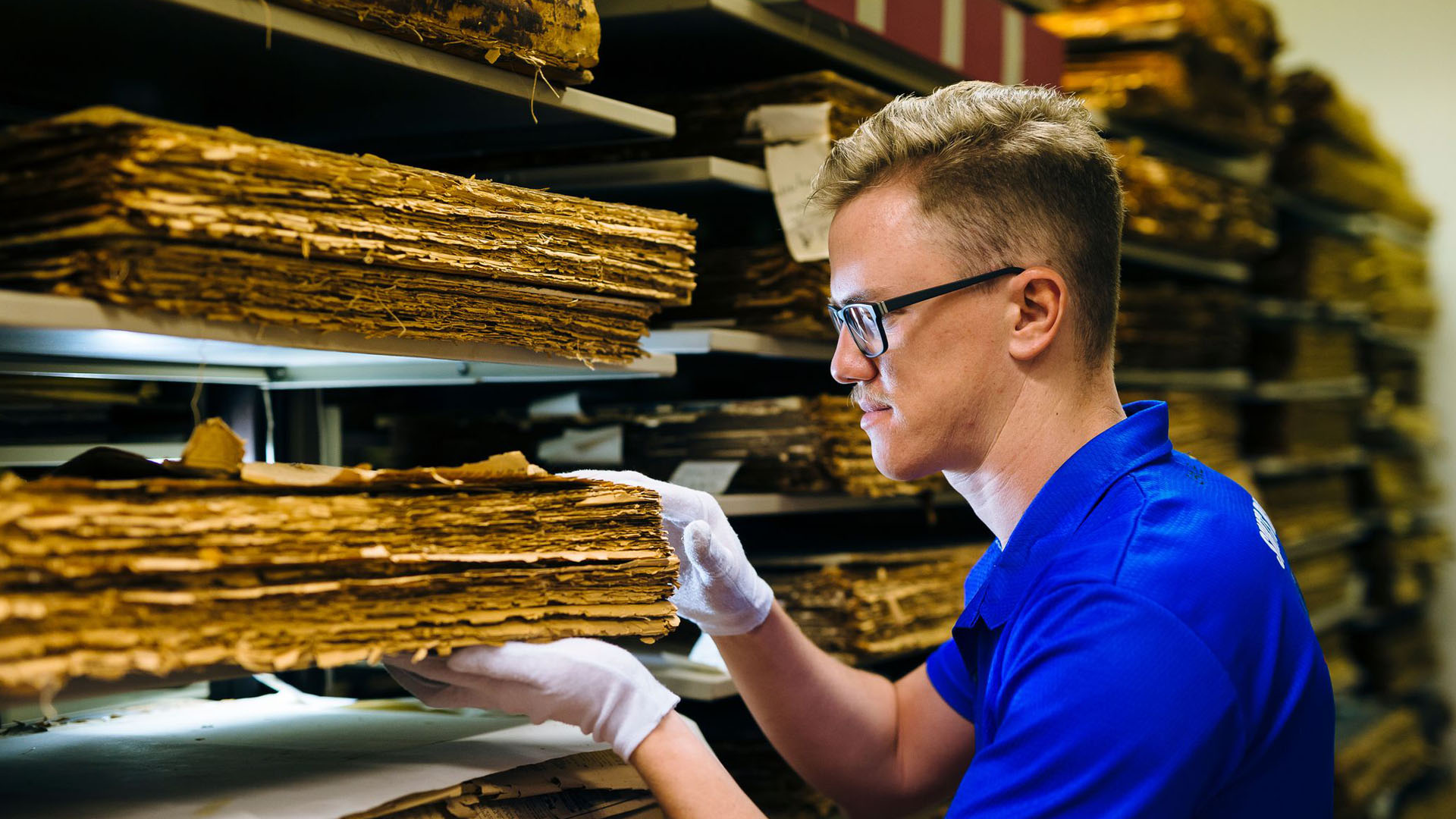 A History student wears gloves as he handles historical documents in an archival room. 