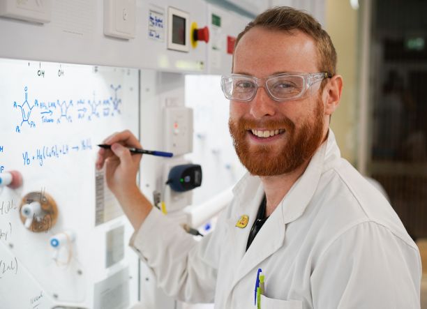 Angus Shephard standing next to a whiteboard with chemical equations on it.