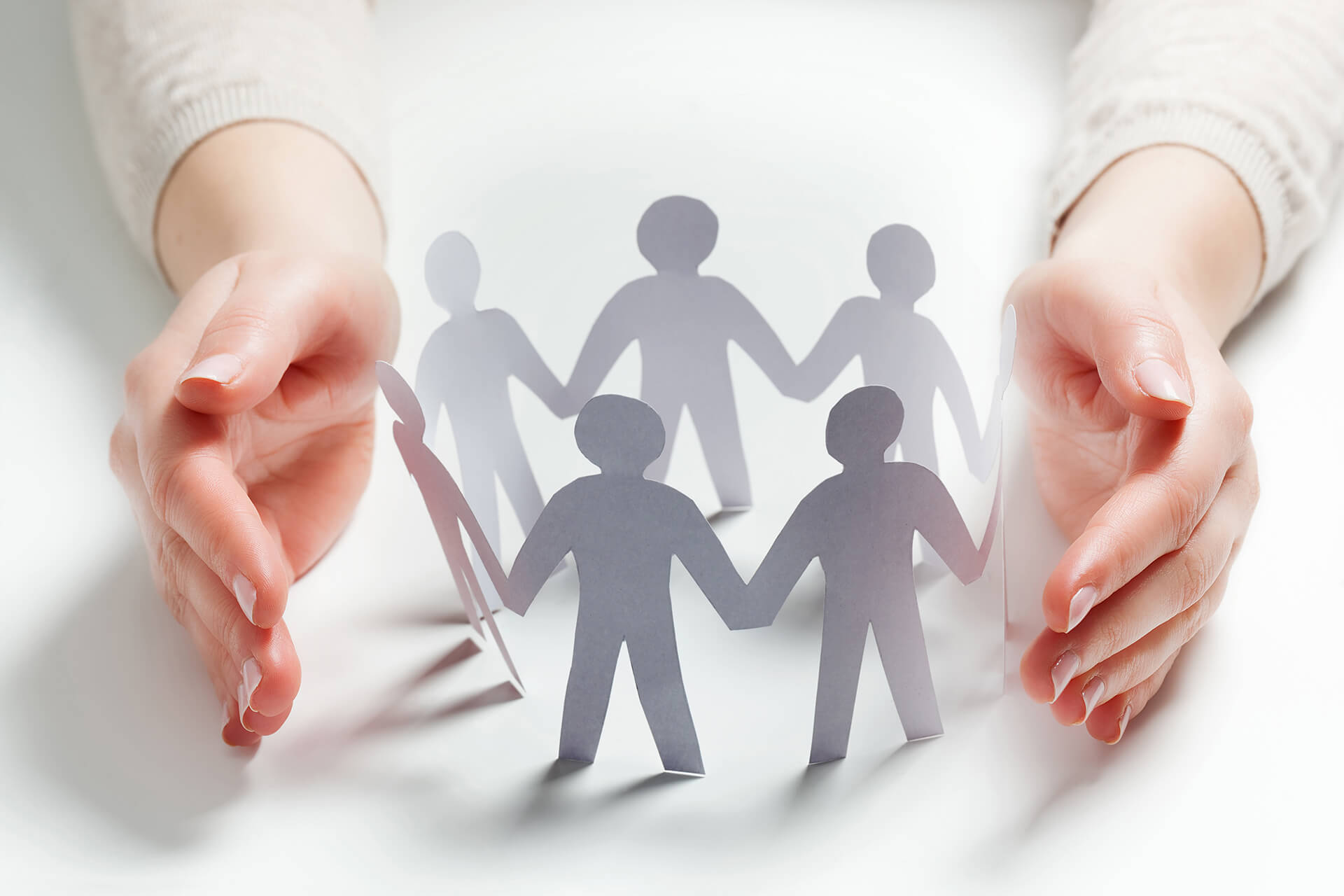 Paper people surrounded by hands in gesture of protection