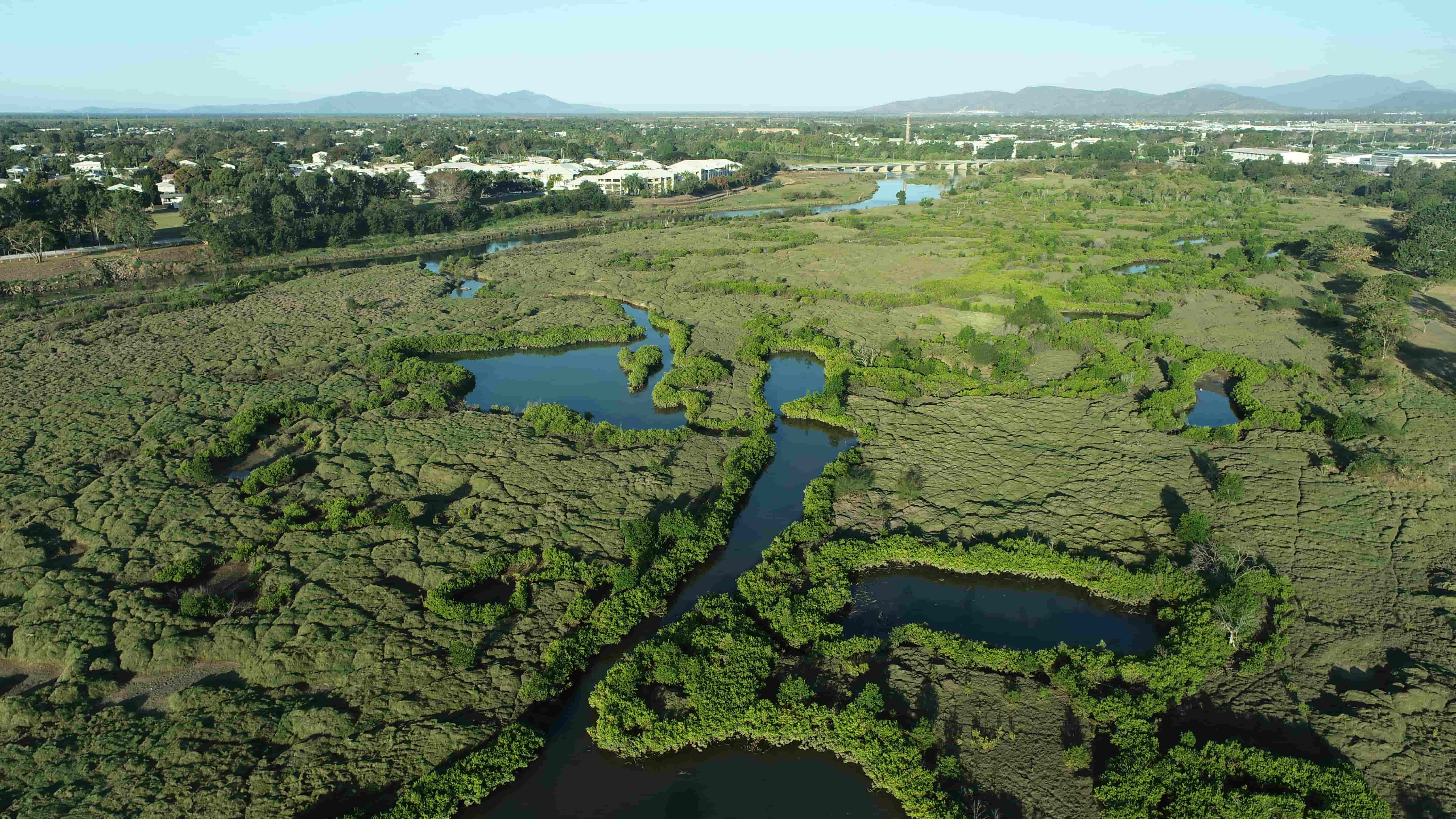 View of wetlands and river in Townsville from above with some buildings and mountains in the distance. 