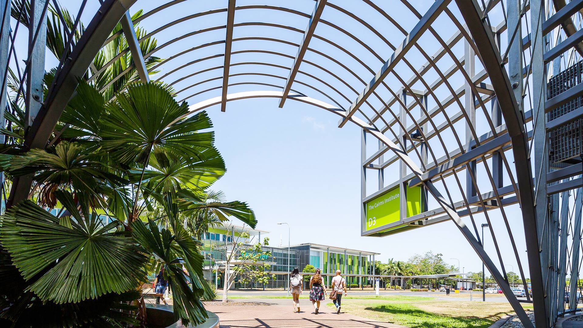 Three people walking in the distance with the Cairns Institute in the foreground. 