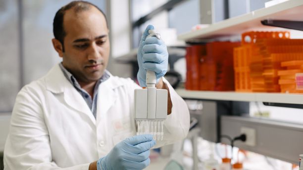 A man wearing a lab coat holds up a piece of scientific equipment. 