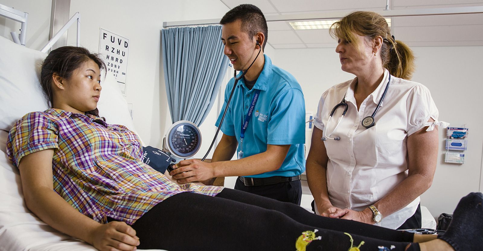 A medical student, supervised by a clinical teacher, checks a patient's blood pressure