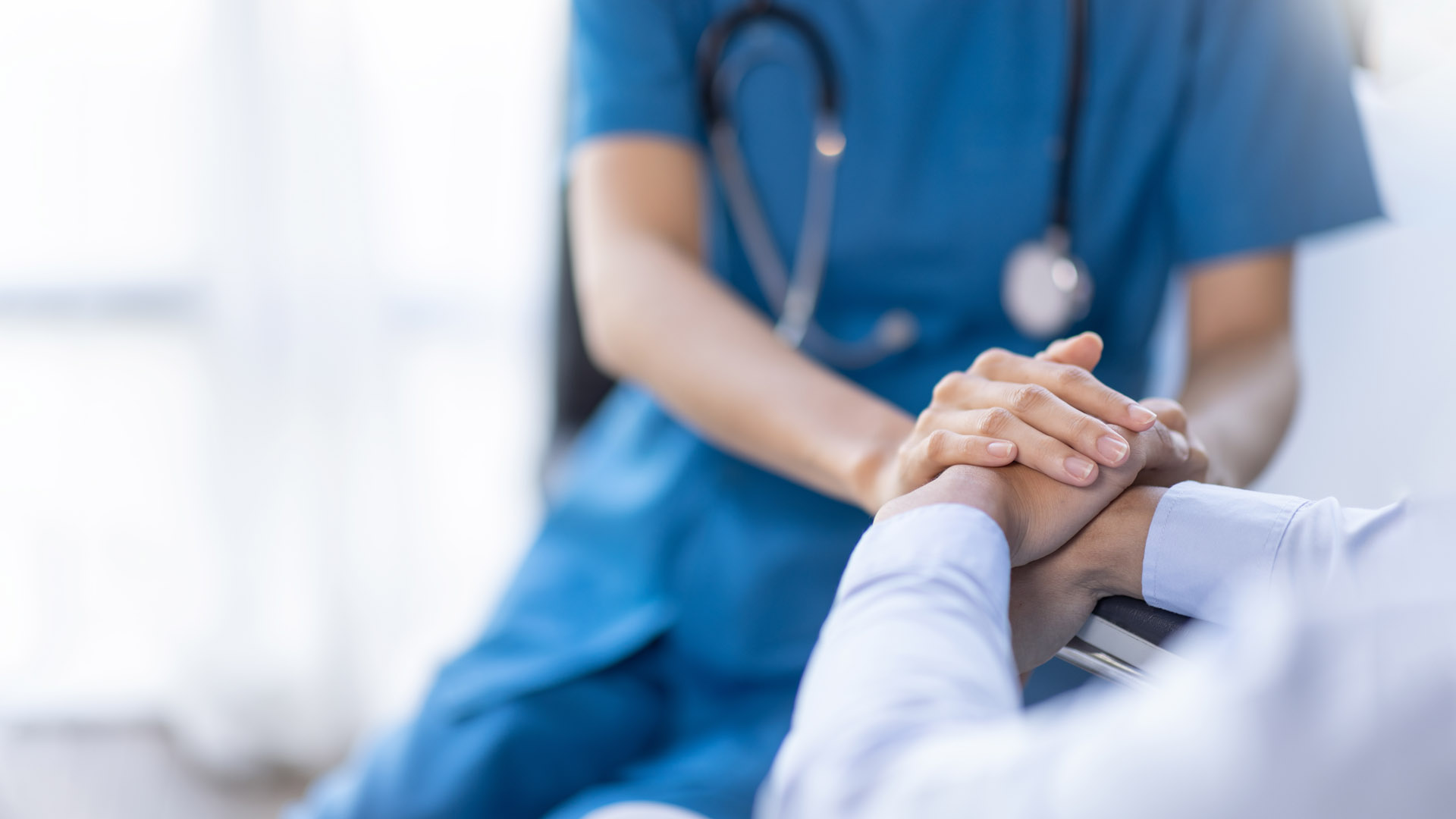 A nurse holds the hand of their patient. Only torso and hands are visible.