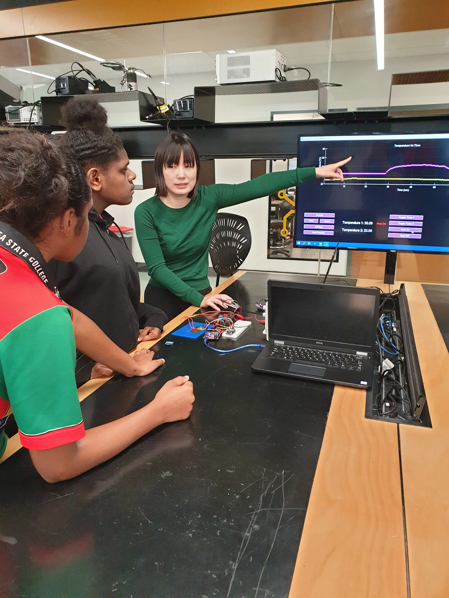 A JCU lecturer and two students examining a computer screen, with an electronic device sitting on a table alongside them. 