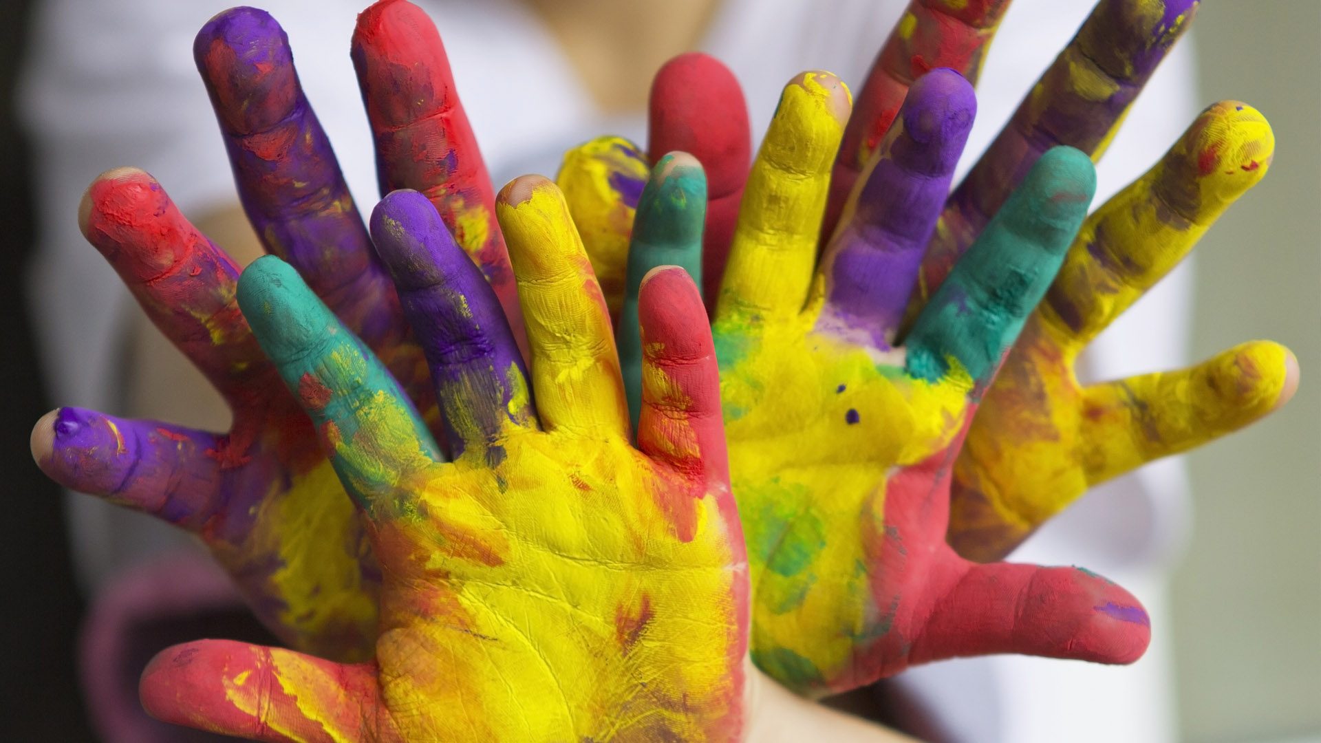 A collection of paint-covered childrens' hands next to each other with palms facing the camera. 