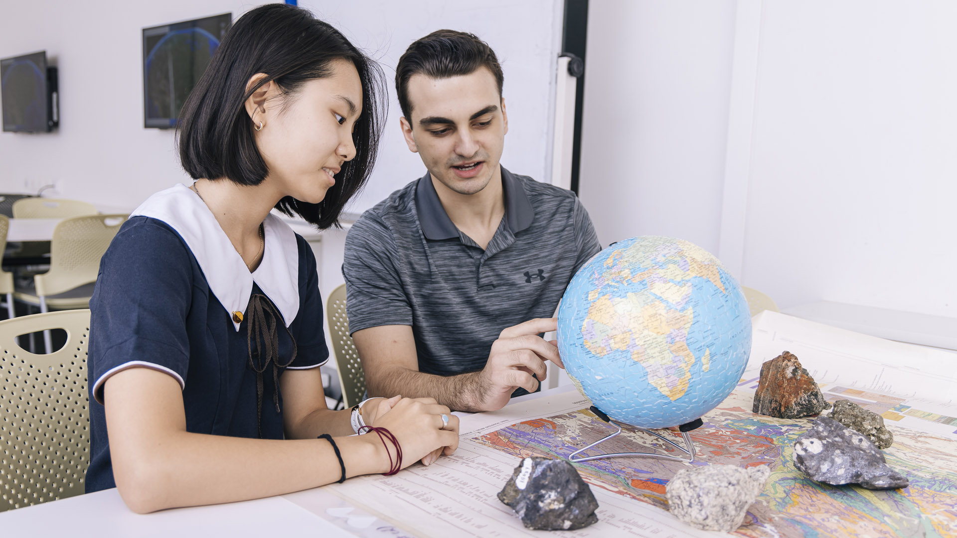 A JCU Education student works on geography with a student, pointing to a globe. 