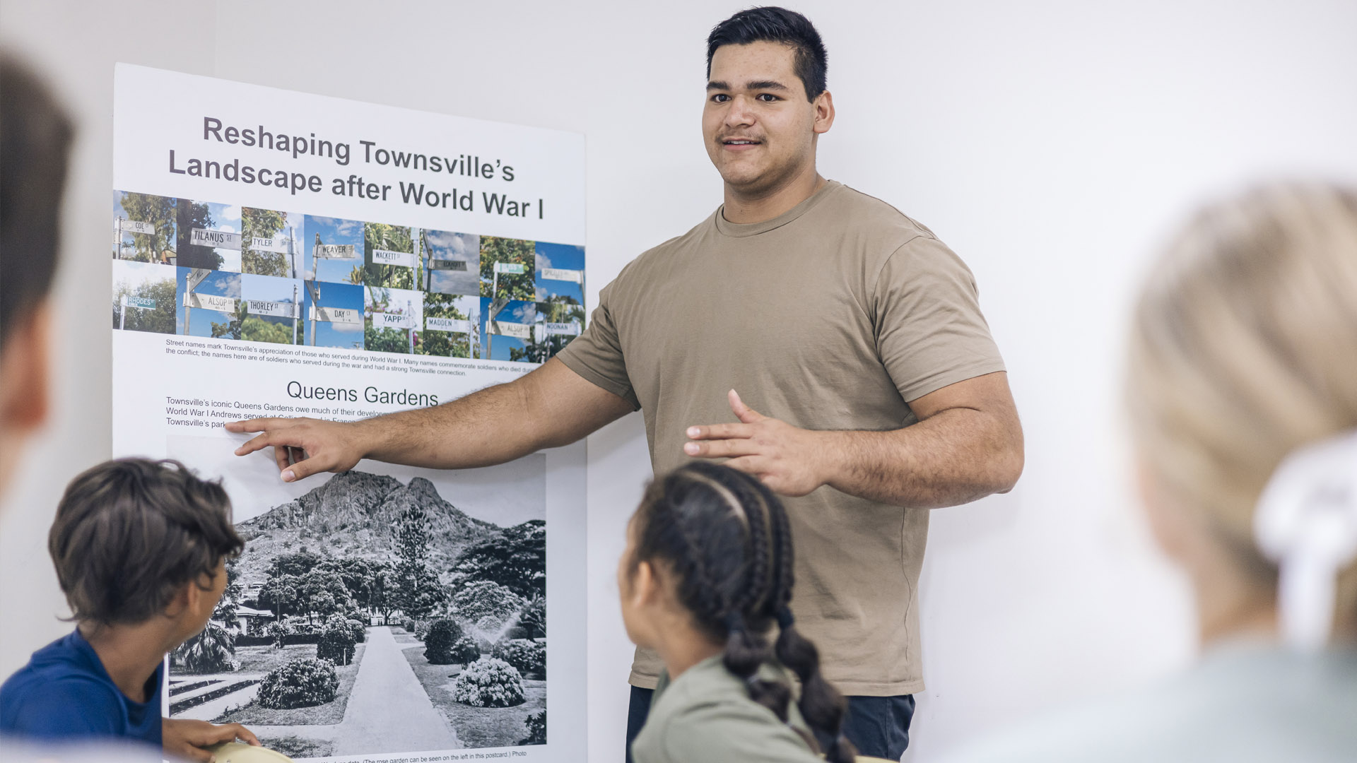 A JCU Education student stands in front of a classroom with students, pointing to a poster. 