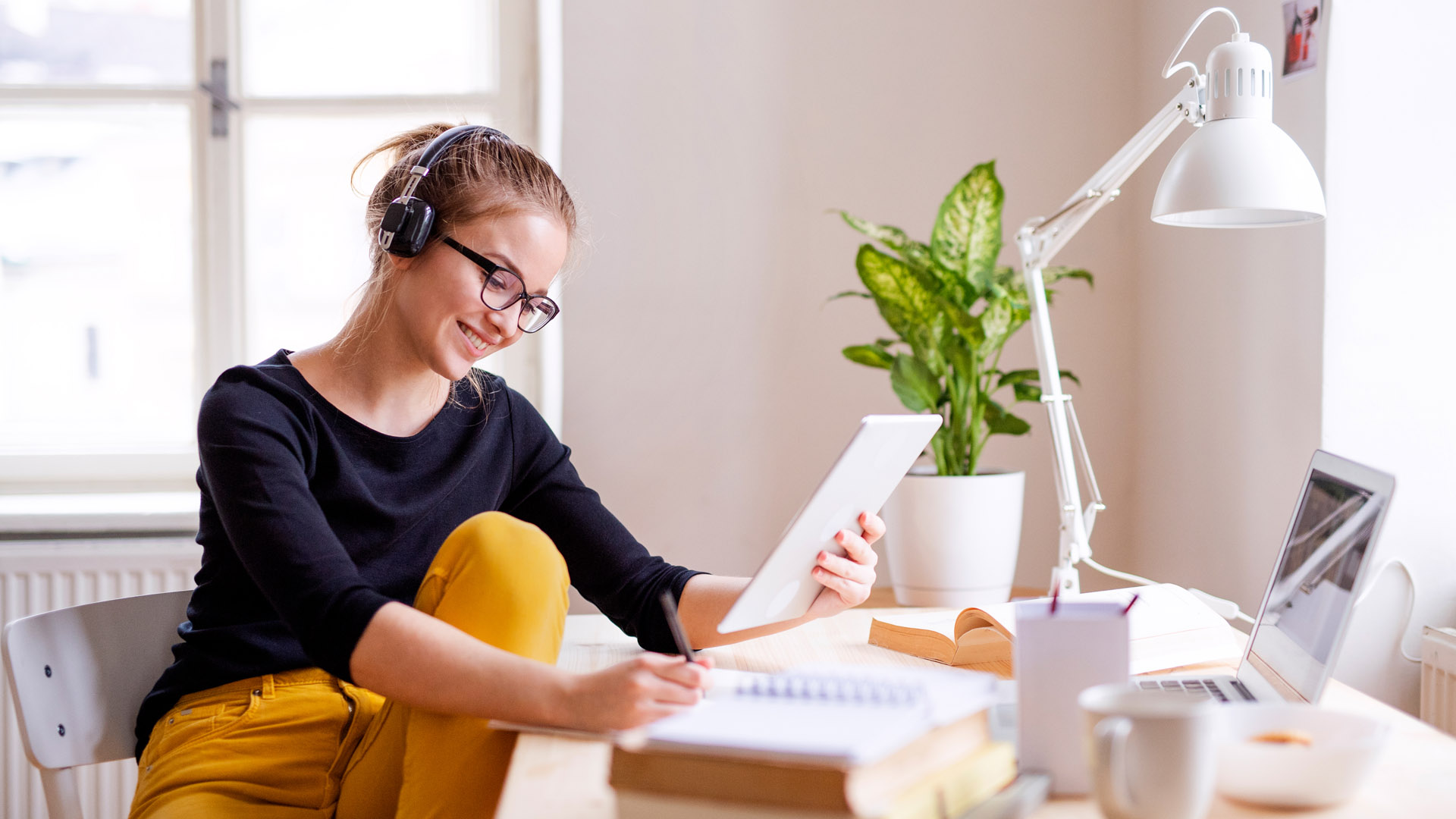 A university student sits at a desk studying, wearing headphones