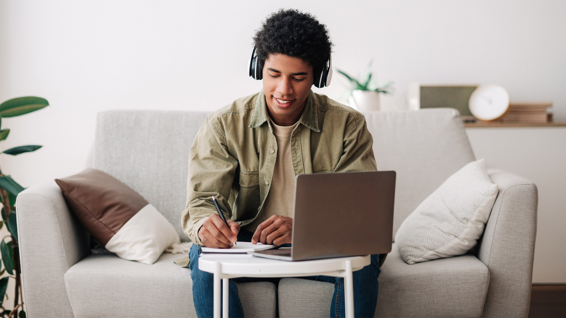 A university student sits on a couch studying using a coffee table. 