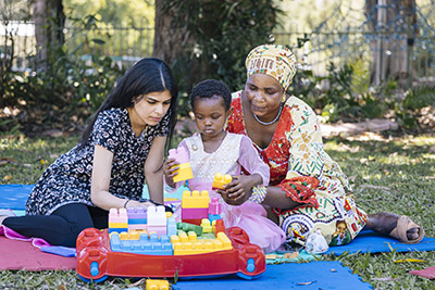 A JCU Social Work student sits outside on a picnic blanket building blocks with a child and their mother. 