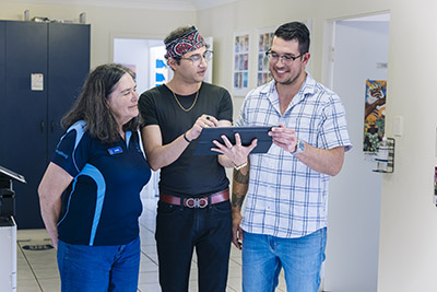 Two JCU Social Work students and a lecturer stand in a hallway having a workplace discussion while looking at an iPad that one is holding. 