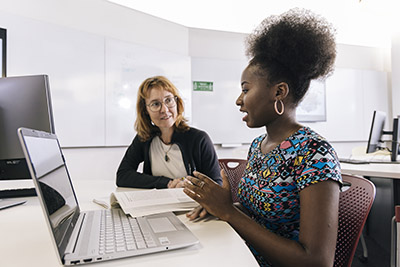 A JCU Social Work student sits with a lecturer receiving study advice, their laptop and textbook on the desk in front of them. 