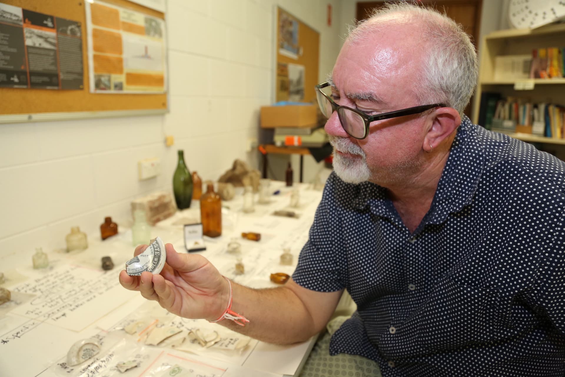 James Cook University archaeology lecturer Dr Nigel Chang examines part of a lid from a 19th century toothpaste container from the 1880s from during excavations at the back of Townsville’s Stanton House.