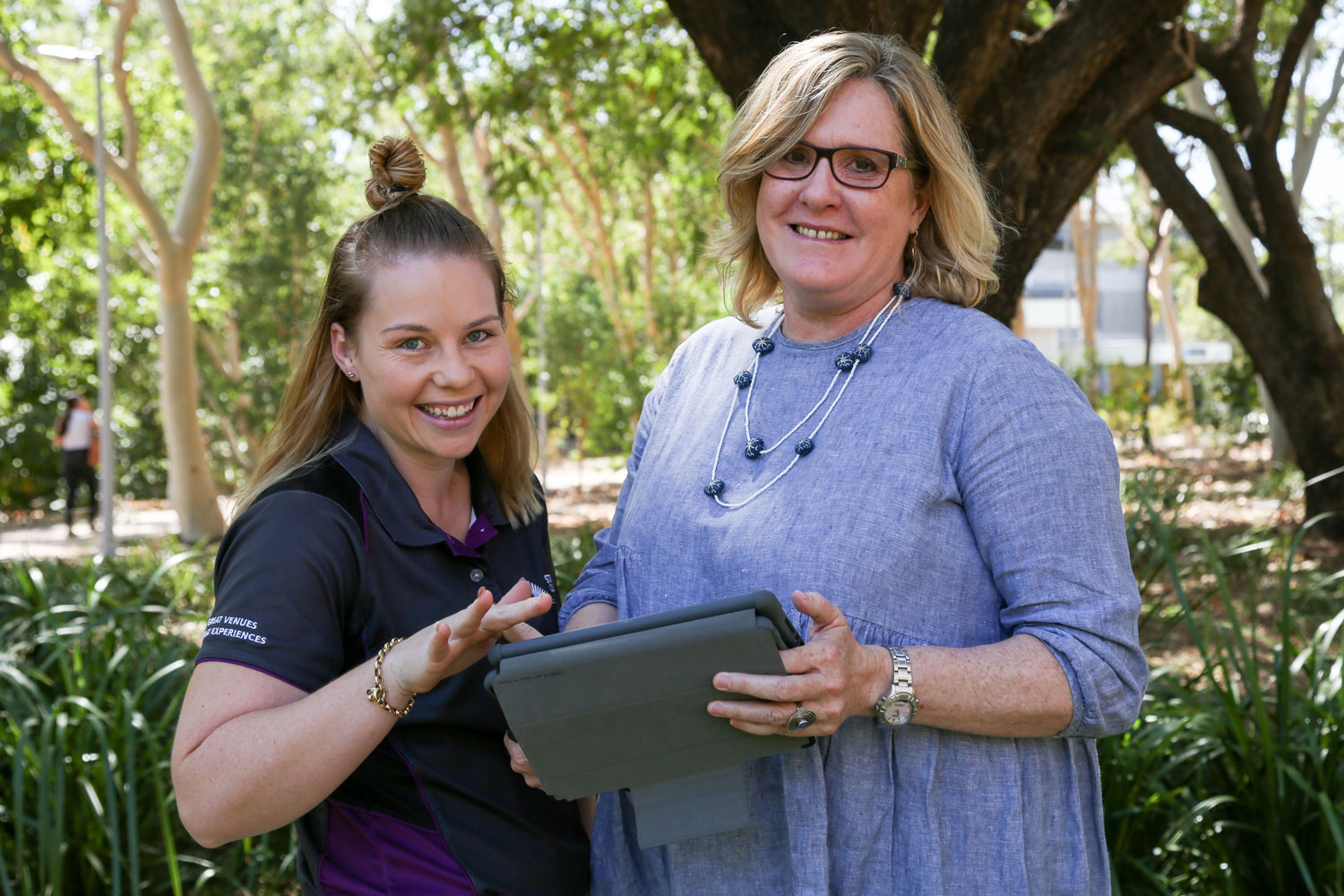 Kelsey touches the screen of an tablet that's being held by Laurie. Both are looking up smiling at the camera