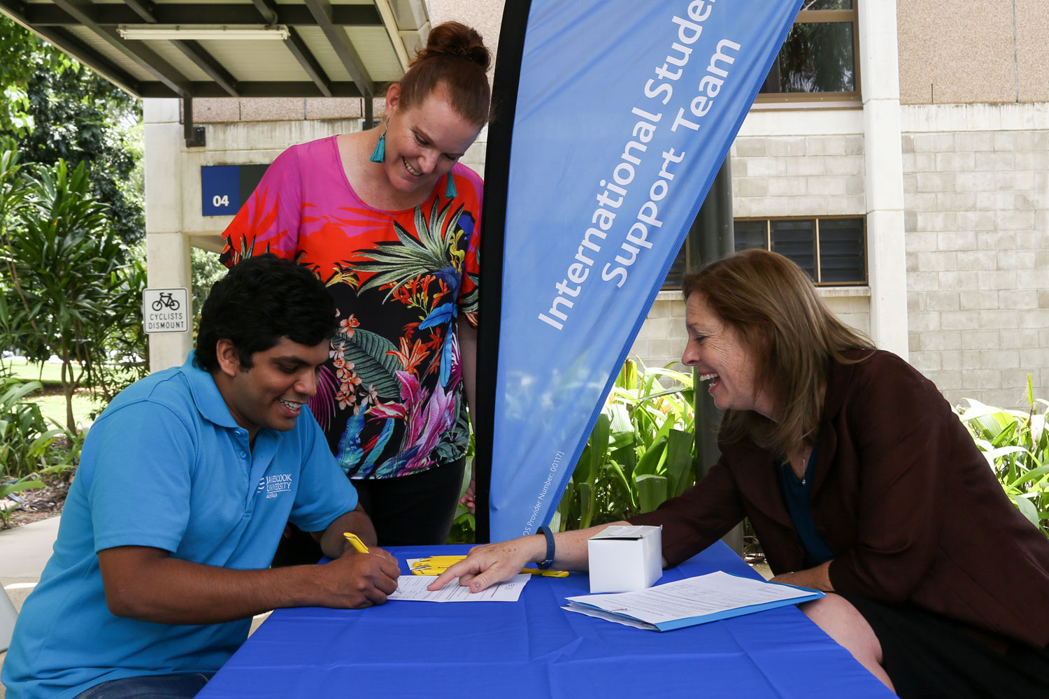 Student fills in forms at a table while two staff members assist him
