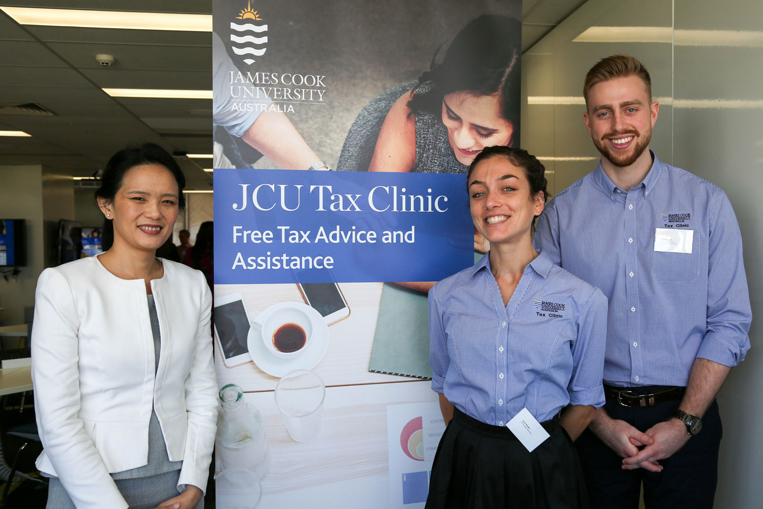 A staff member and two students stand next to a banner advertising the Tax Clinic