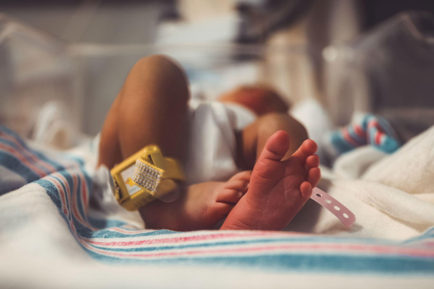 The feet of a newborn baby who is lying in a hospital cot, wearing hospital tags around ankles
