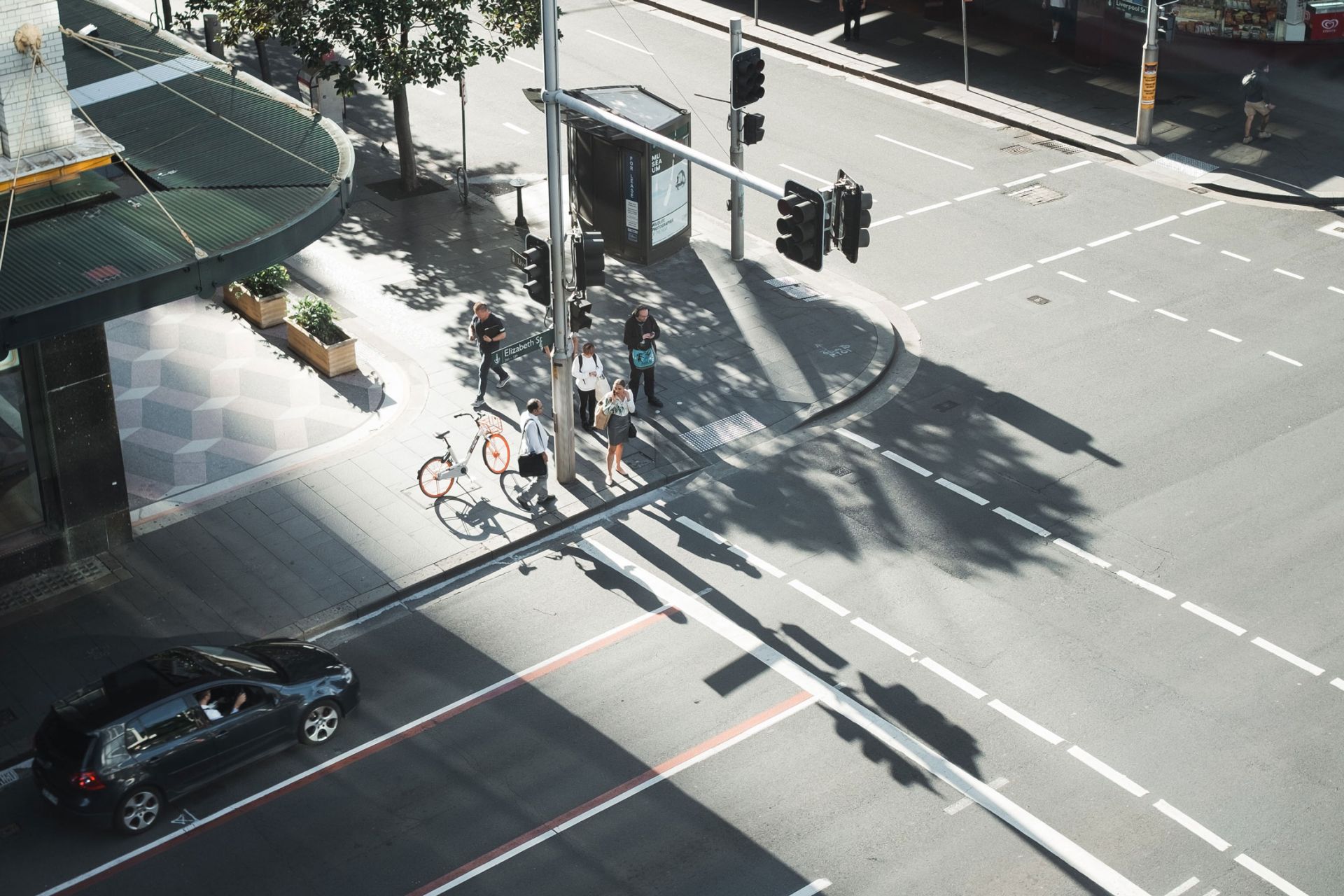Looking down from height to an intersection in the city; people waiting at lights, car coming