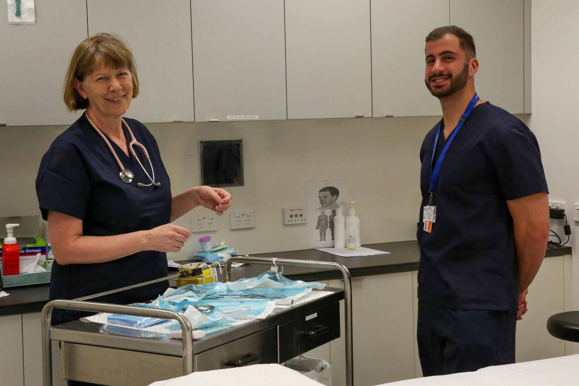 Peta-Ann and Elie stand in a treatment room, next to a tray of equipment