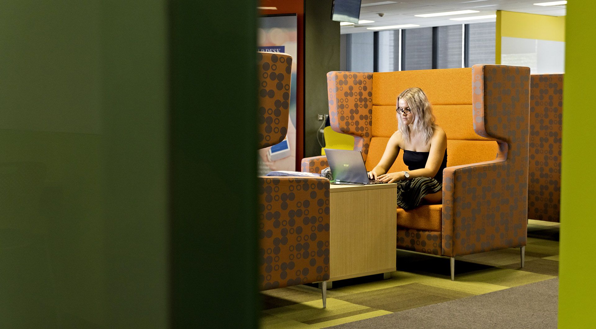 A female students sits in a booth looking at a laptop