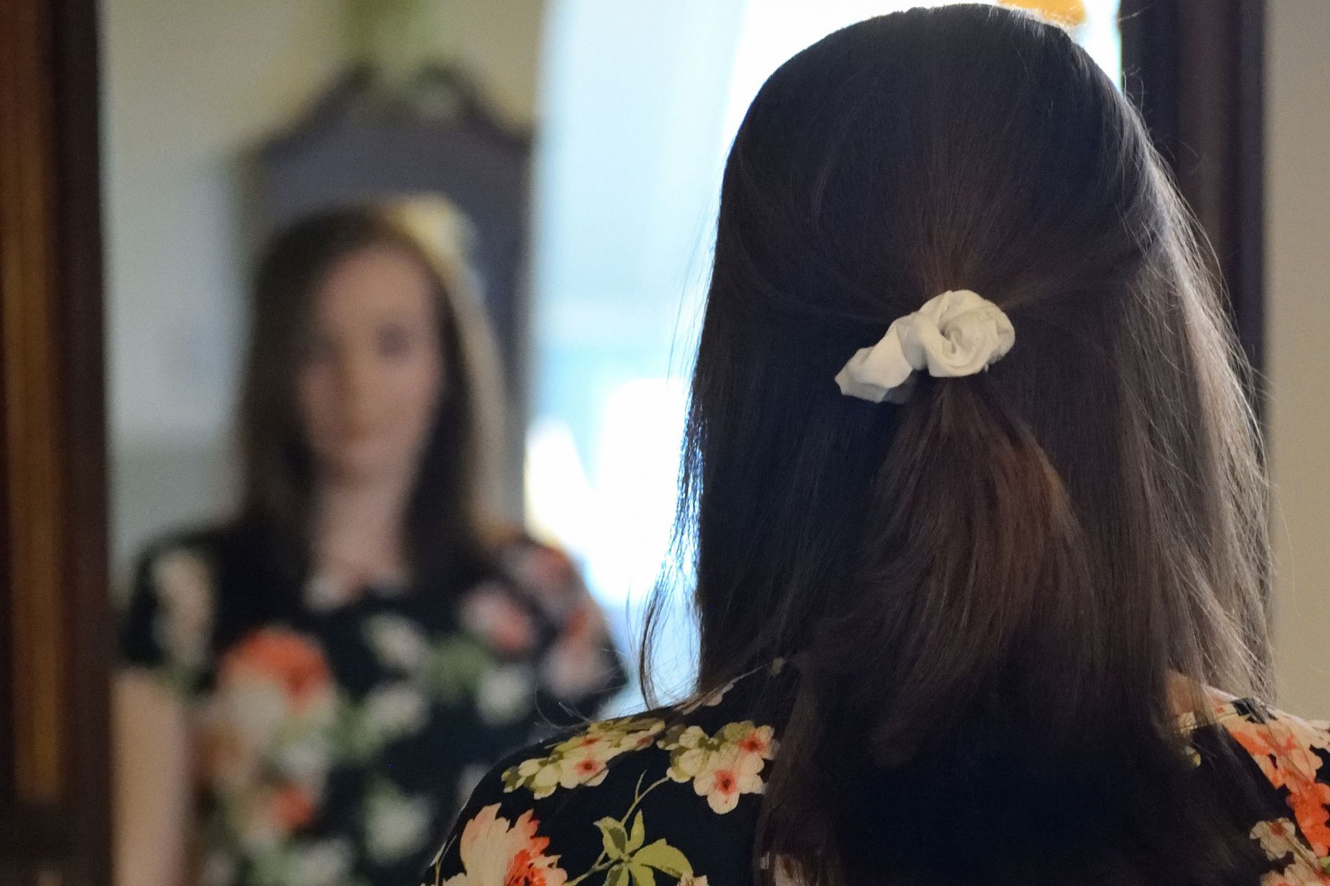 A woman looking into a mirror, as seen from the back of her head