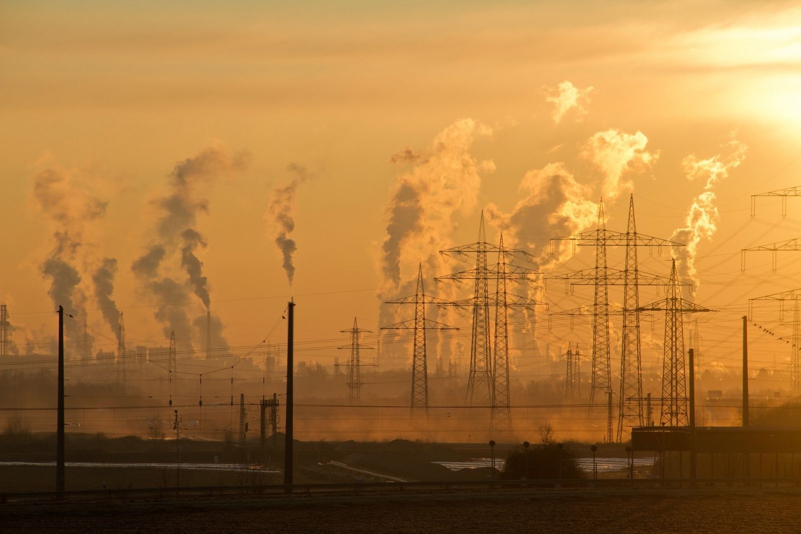 Power lines and smoke stacks against a smoggy sunset