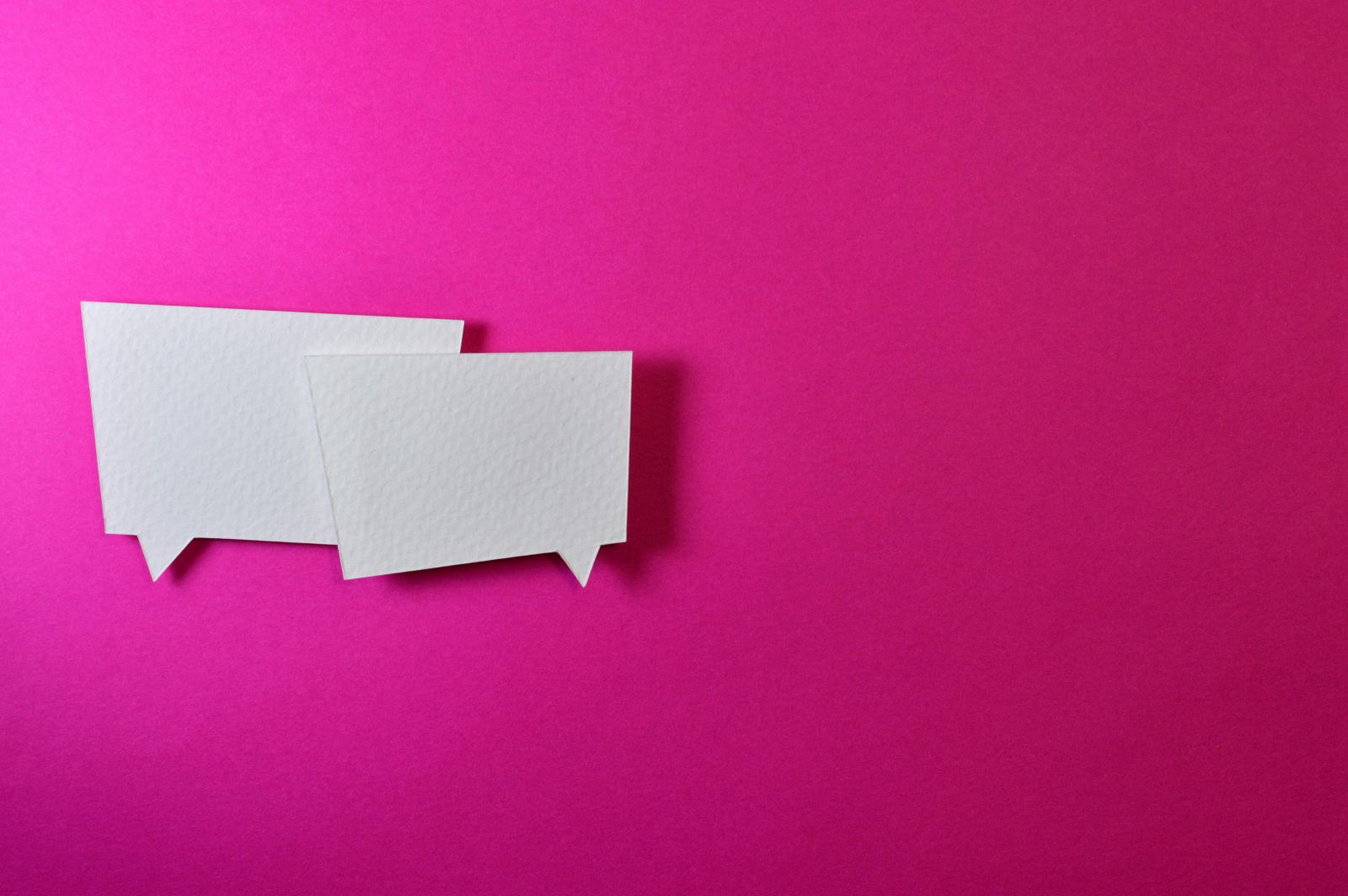 An image of two white speech bubbles with a solid pink background