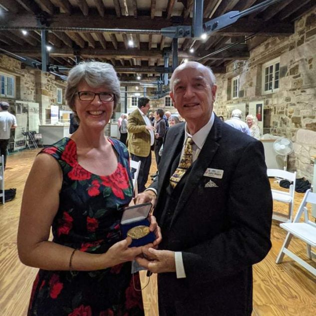 JCU Special Collections Manager Bronwyn McBurnie stands smiling next to Emeritus Professor John Pearn while they hold a gold medal.