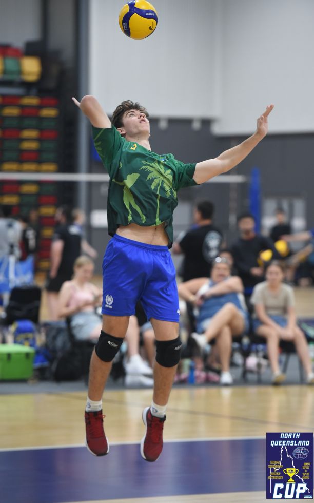 An action shot of Benson jumping in the air while hitting a volleyball over the net on an indoor volleyball court as a crowd watches on.