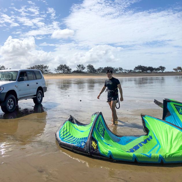 Man and four-wheel-drive on beach with kitesurf