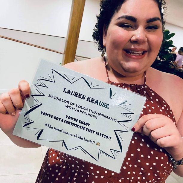 Lauren Krause smiling while holding the mock graduation certificate her friends made for her. 