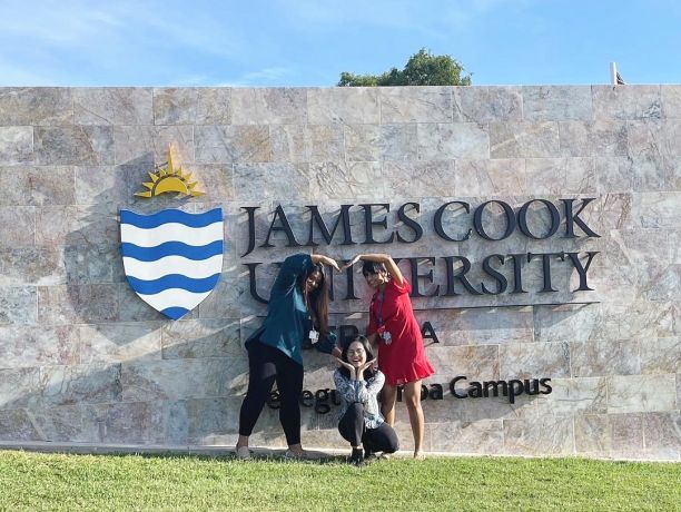 Three graduates forming heart in front of JCU sign