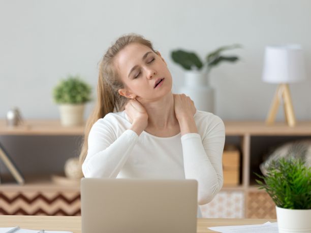 A female clutches her sore neck at a desk. 