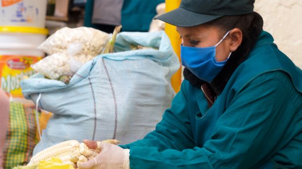 A Peruvian vendor wearing a mask while cleaning corn.