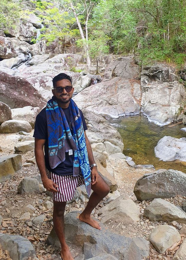 man in sunglasses with towel over shoulder standing on rocks at a waterhole
